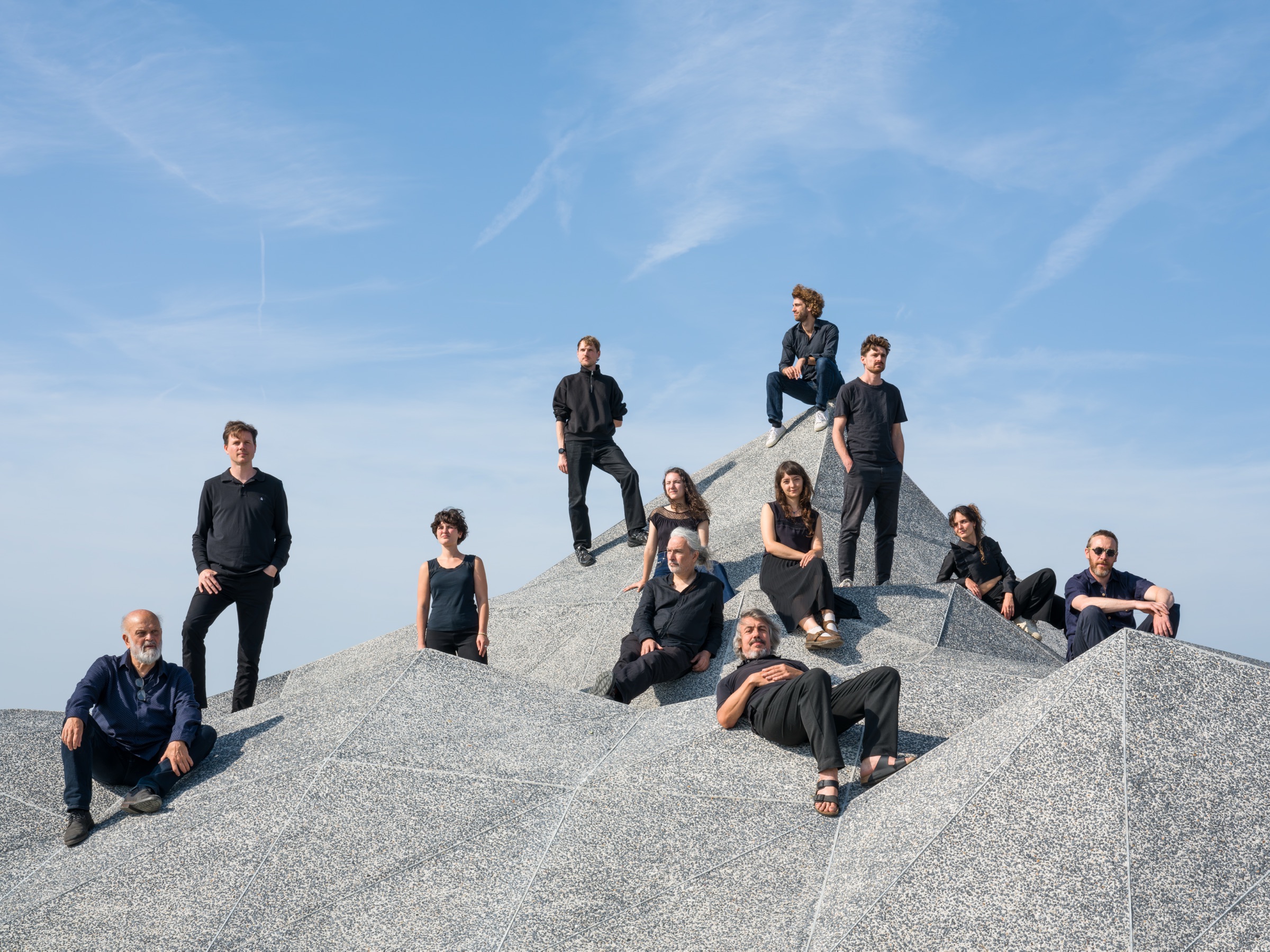 De leden van het Safety Last Soundpainting Ensemble, in het zwart gekleed, op een granieten rots tegen een blauwe lucht